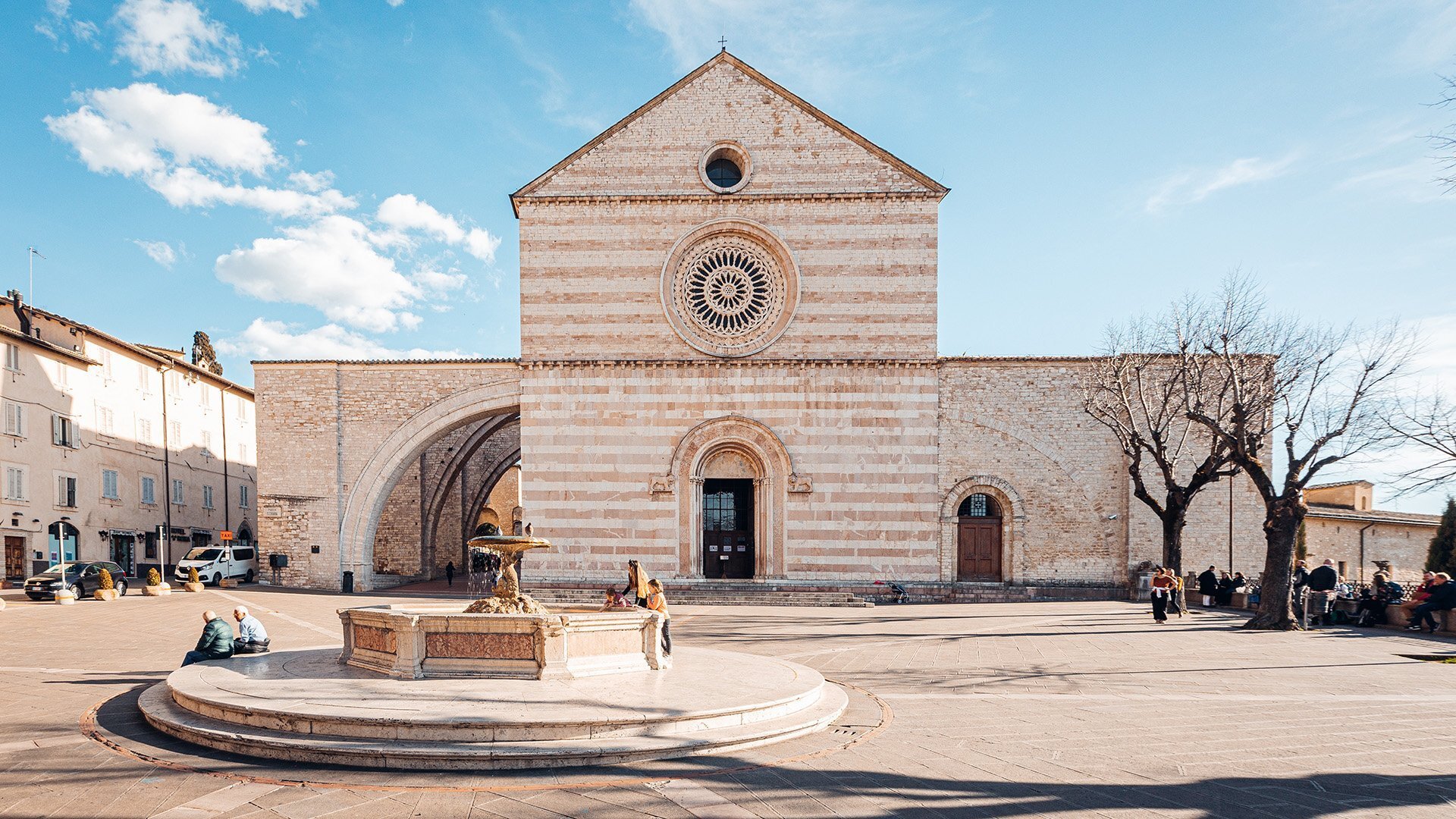 Historic stone church with fountain and people seated nearby.
