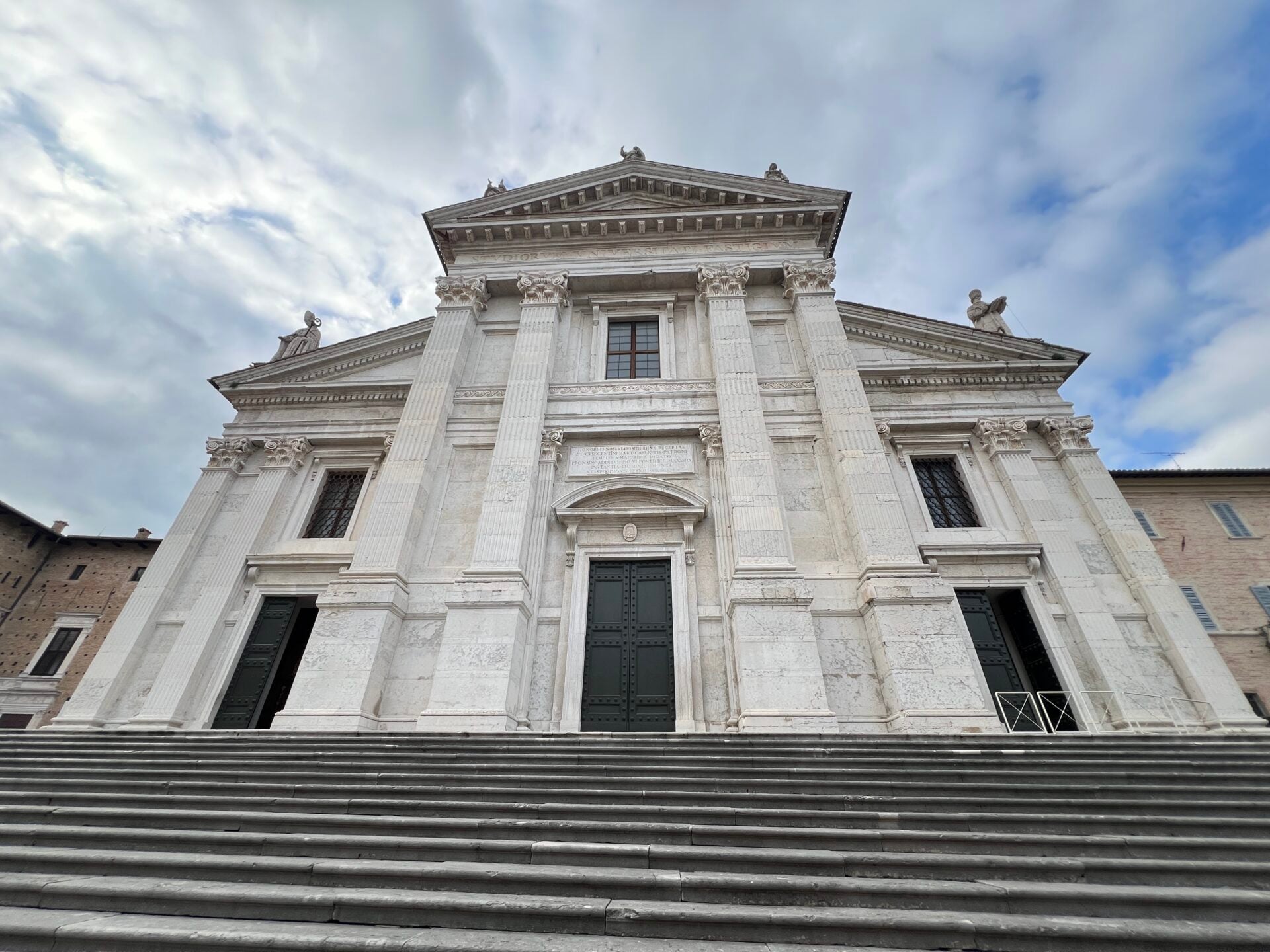 Historic cathedral with grand staircase and cloudy sky.