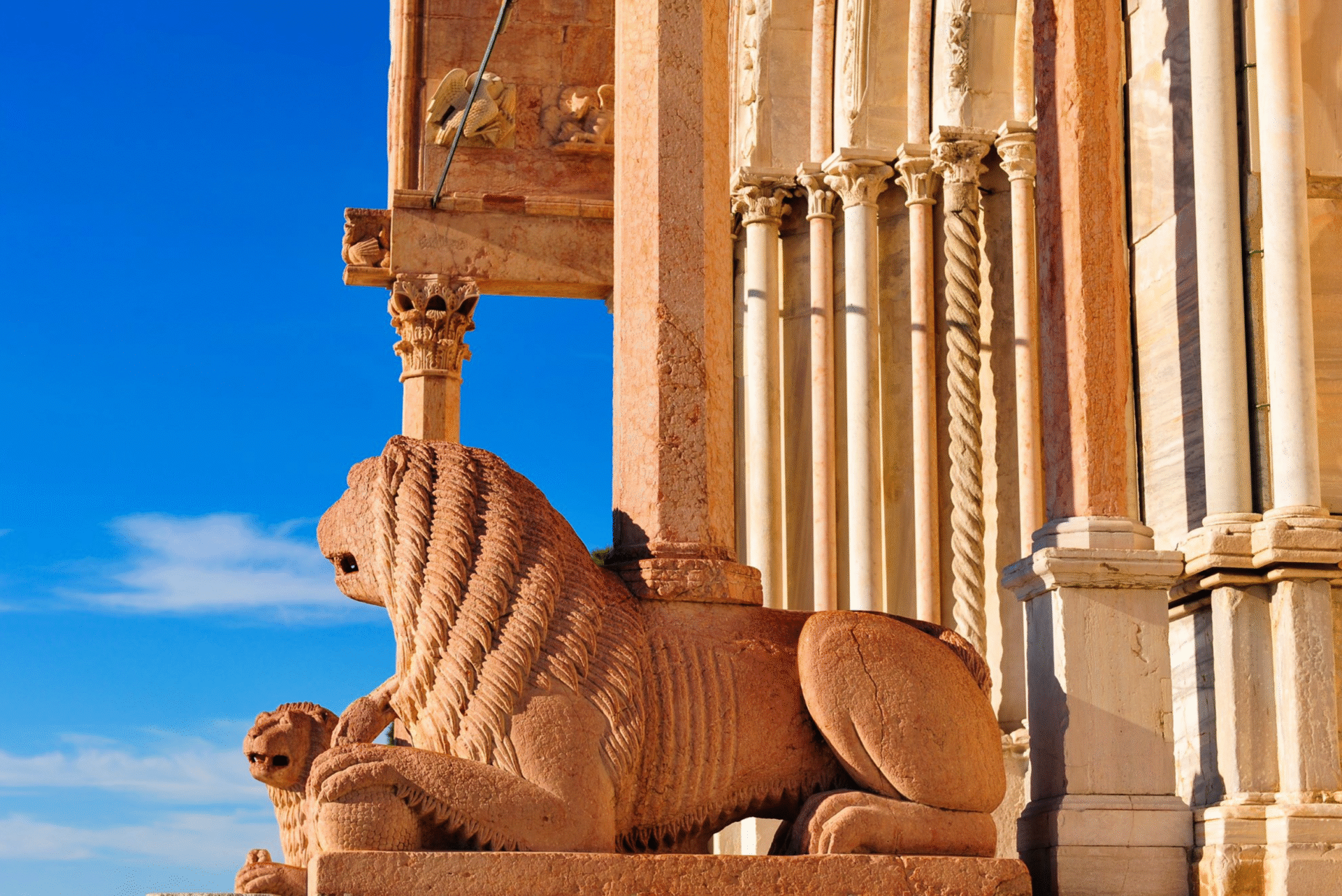 Ancient lion stone statue near columns at sunset.